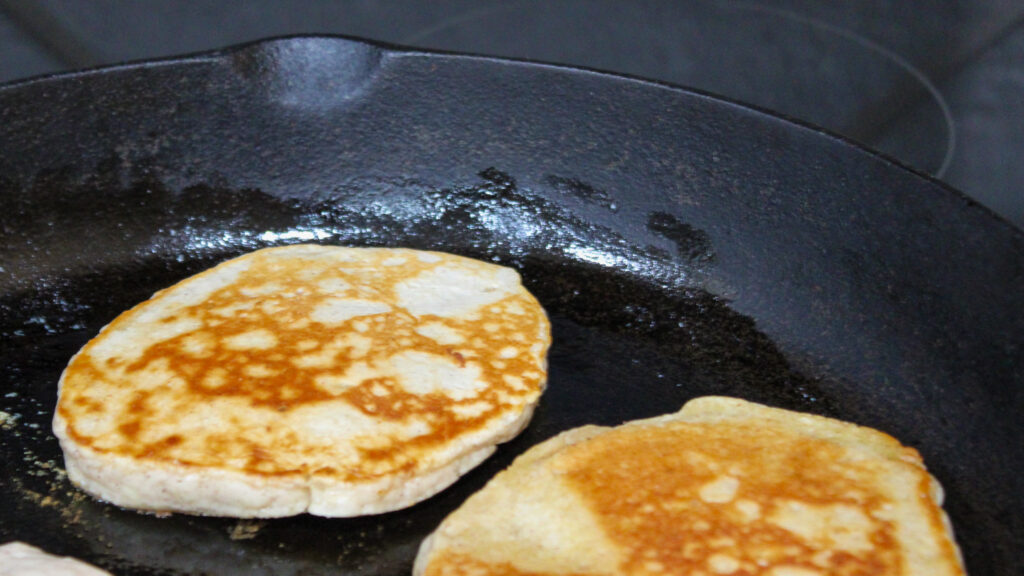 Pancakes cooking in cast iron skillet.