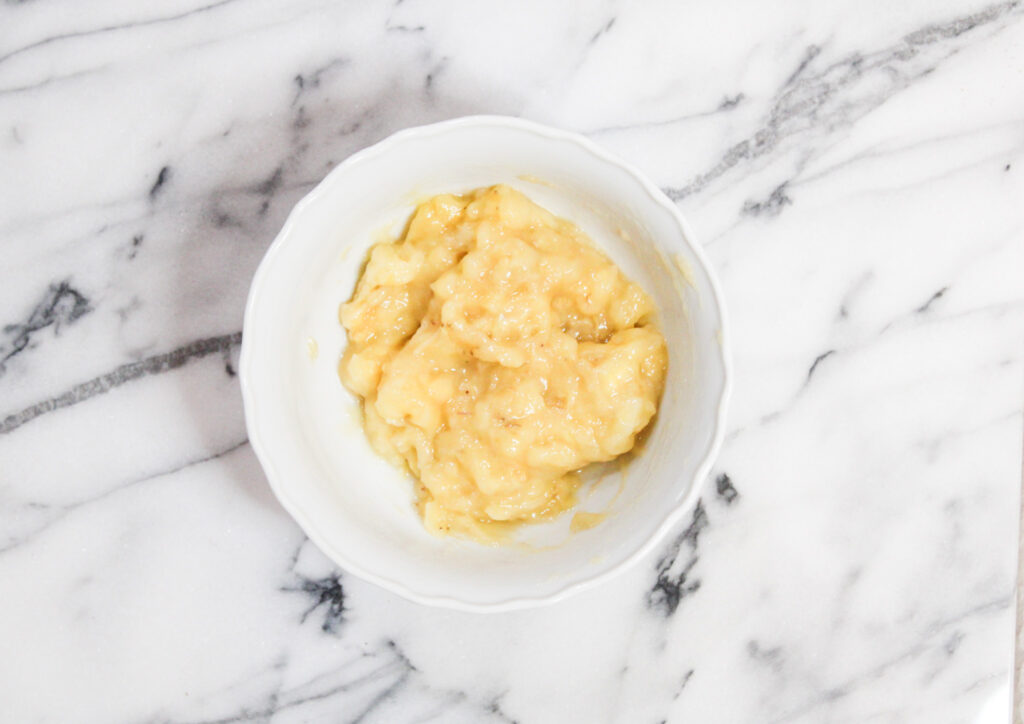 Mashed bananas in white bowl sitting on marble countertop. 