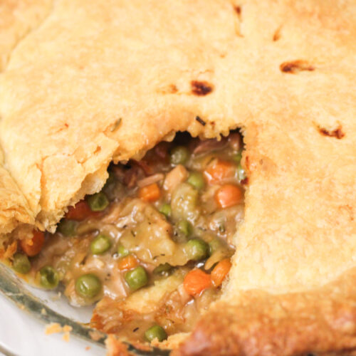 Homemade Chicken Pot Pie with slice removed so you can see carrots, peas, and cooked ingredients.