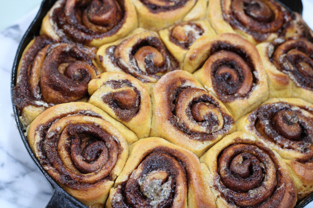 Baked but unfrosted pumpkin cinnamon rolls in cast iron pan. 