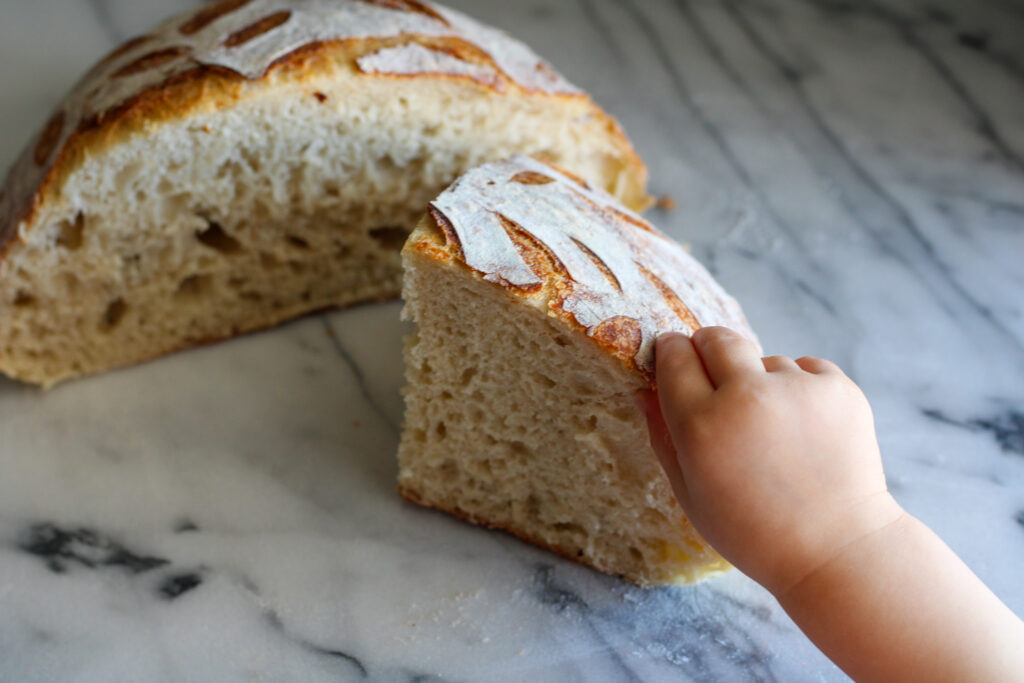 Small child's hand grabbing section of artisan sourdough bread.