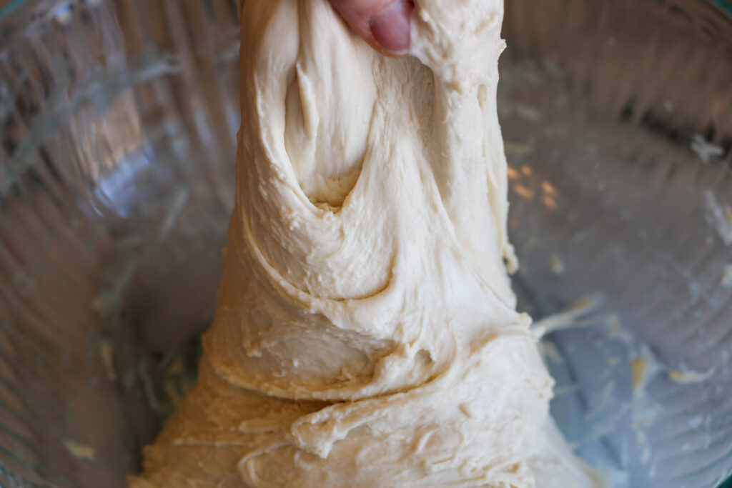 Stretching sourdough bread dough in glass bowl.