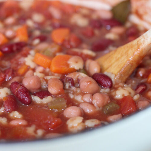 Minestrone soup in white pot with wooden spoon.