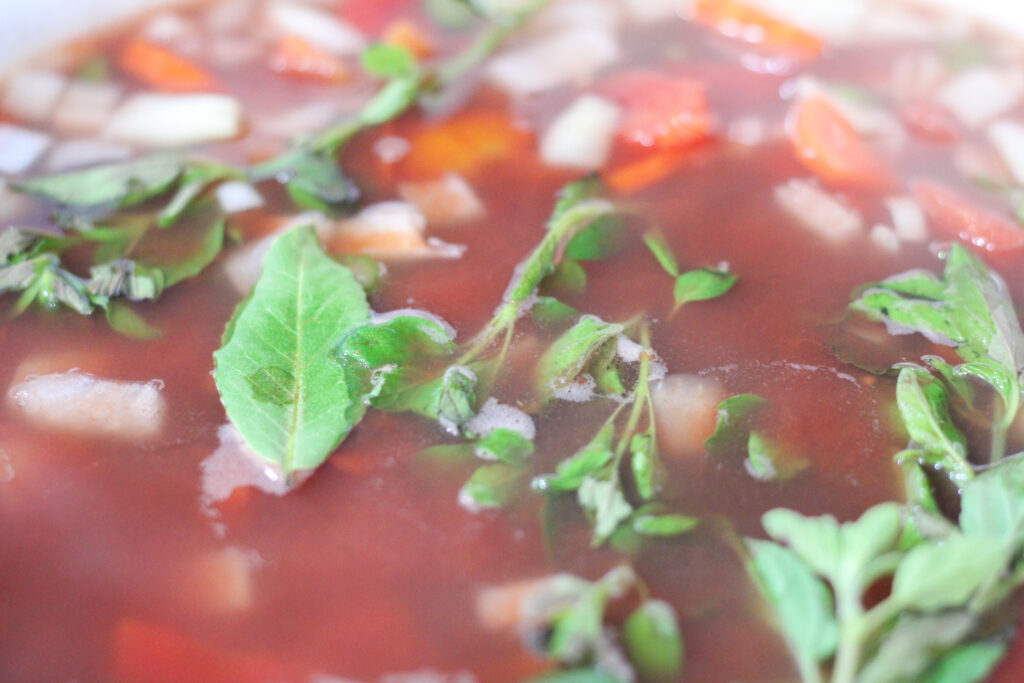 Minestrone soup in white pot with fresh herbs.