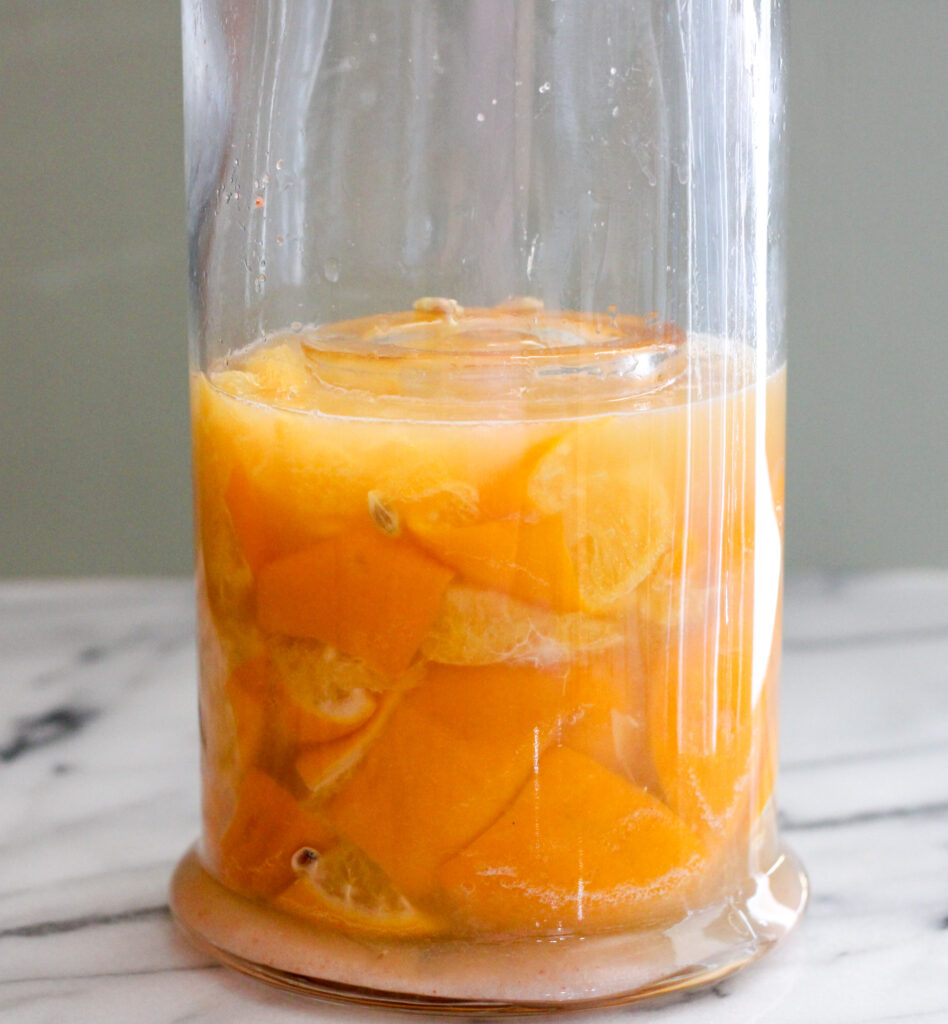 Lemons submerged in juice in a glass jar.