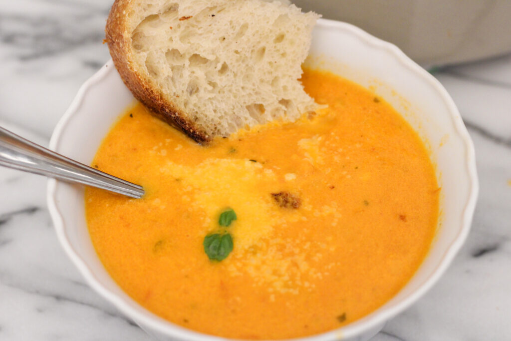 Bowl of tomato soup with bread, spoon and fresh basil.