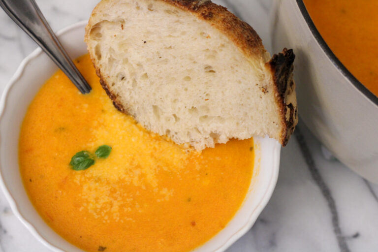 Bowl of tomato soup with bread, spoon and fresh basil.