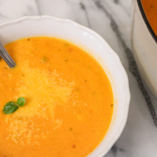 Bowl of tomato soup with spoon and fresh basil.