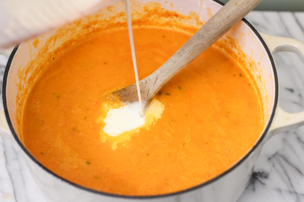 Adding cream to pot of tomato soup with wooden spoon.