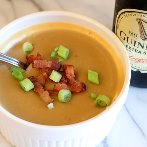 Potato, beer, cheese soup in bowl garnished with bacon and green onion. Bottle of Guinness in background.