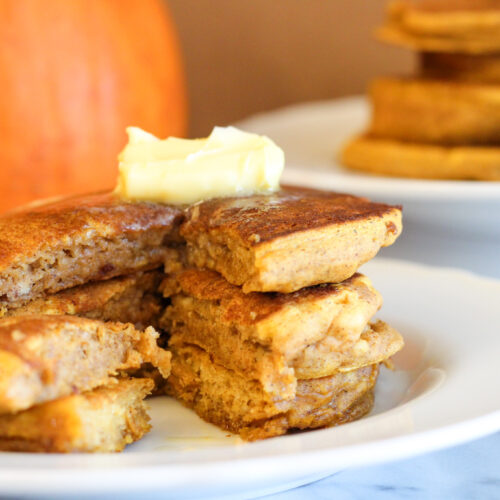 Pumpkin Pancakes with bite missing, butter on top and pumpkin in background.