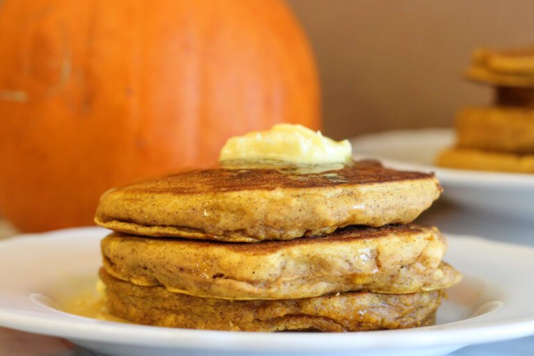 Pumpkin Pancakes with butter on top and pumpkin in background.