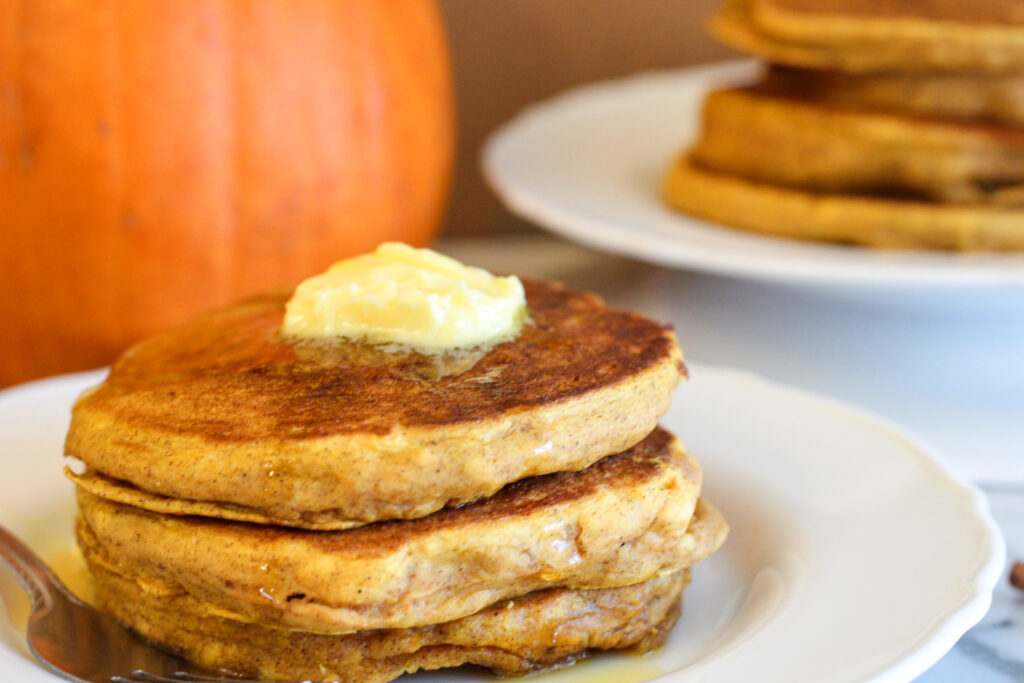 Pumpkin Pancakes with butter on top and pumpkin in background.