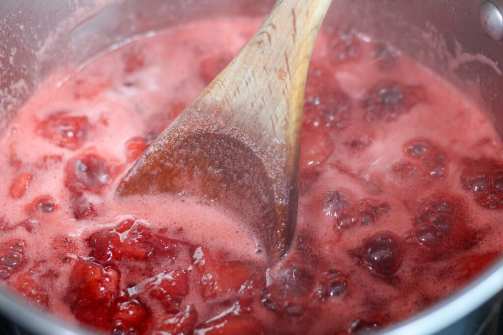 Cooking strawberry jam with wooden spoon
