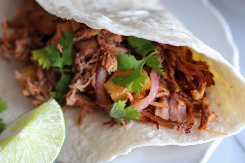 Shredded pork taco on plate with wedge of lime.