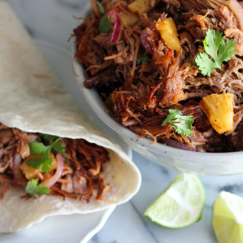 Bowl of tacos al pastor meat and shredded pork taco on plate with wedge of lime.