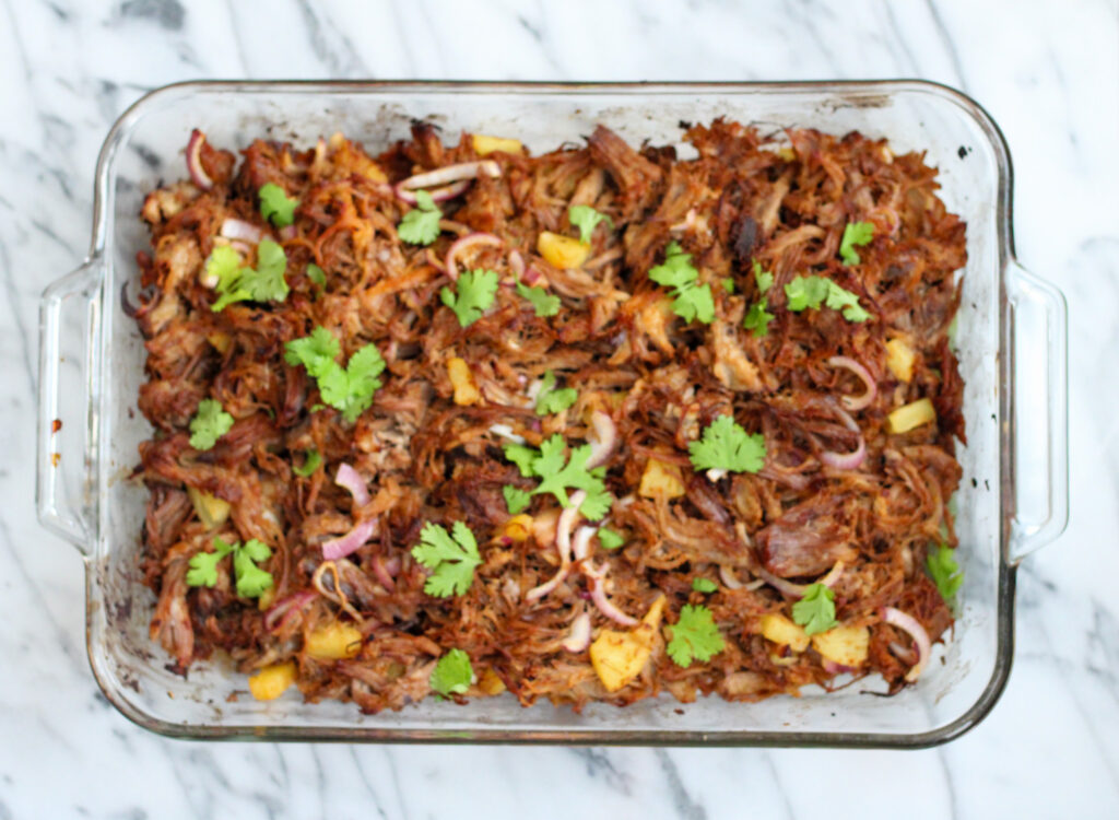 Tacos al pastor meat in glass casserole dish with cilantro garnish.