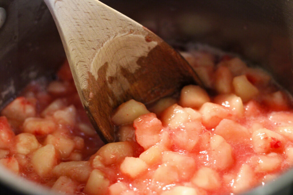 Wooden spoon and peaches in cooking pot.