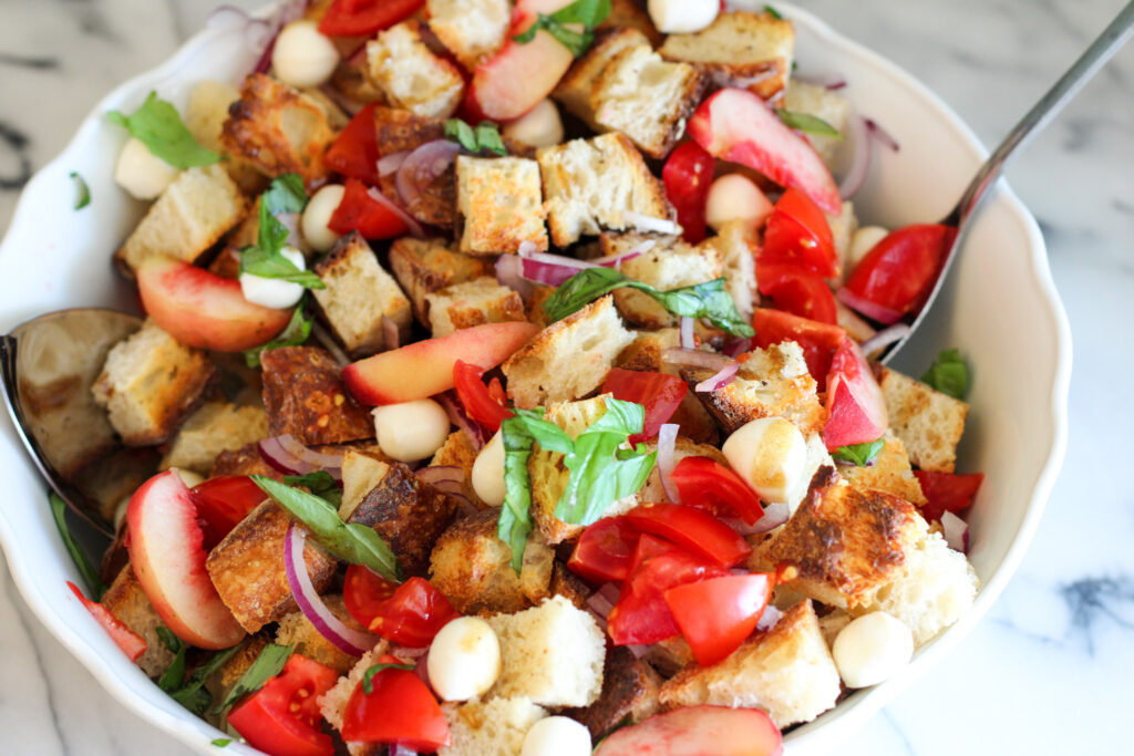 White bowl with peach panzanella salad.