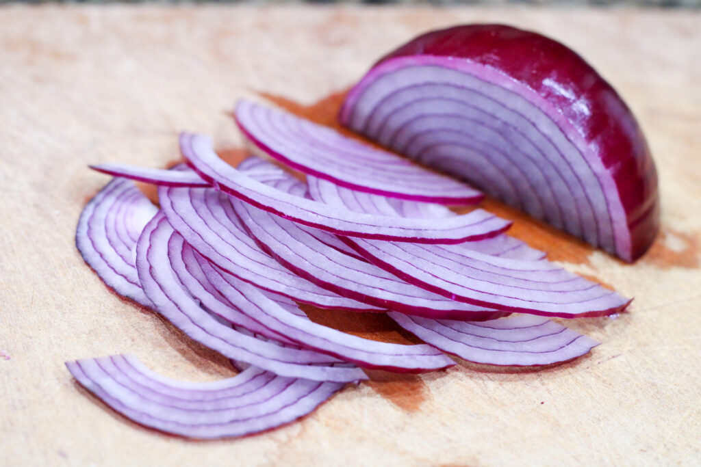 Thinly sliced red onion on cutting board.
