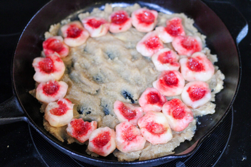 Sliced peaches arranged on sugar in cast iron pan.