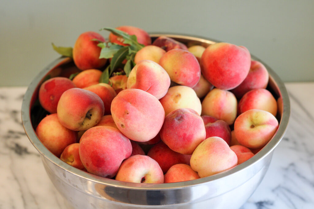 Stainless steel bowl full of fresh peaches.