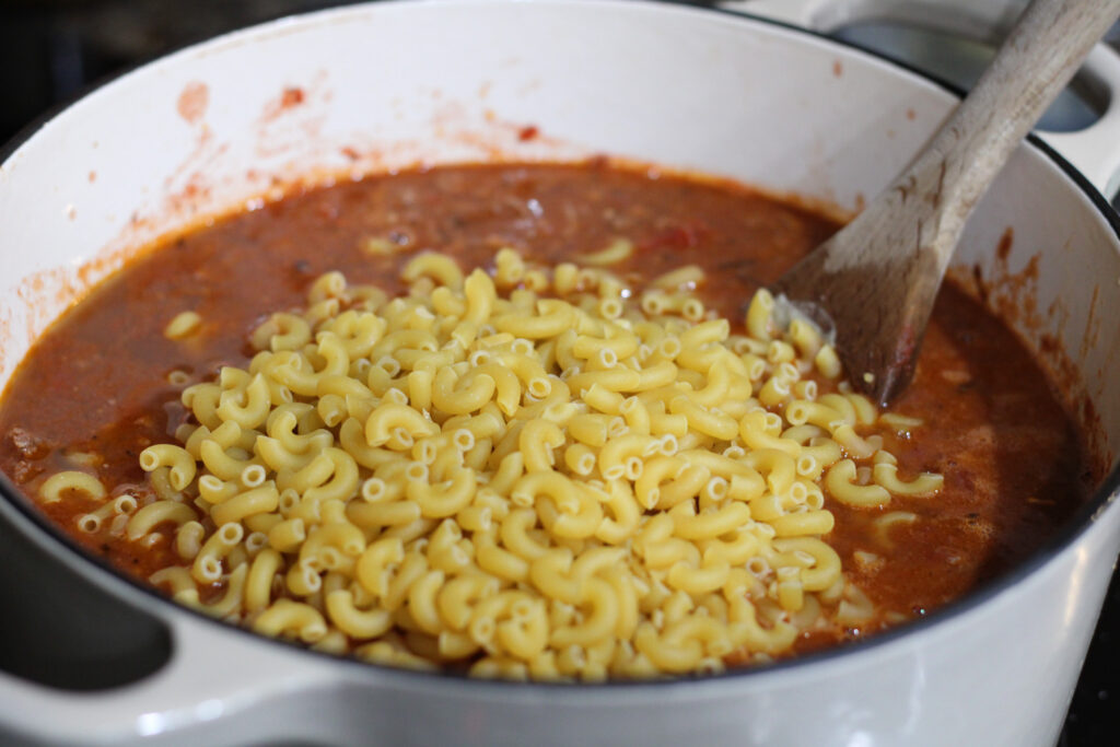 Uncooked macaroni in pot of tomato based meal.
