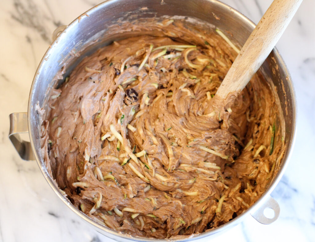 Stainless steel bowl of chocolate batter with shredded zucchini.