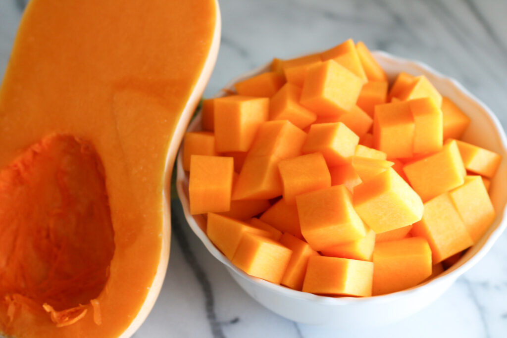 Cubed butternut squash in bowl next to half butternut squash.