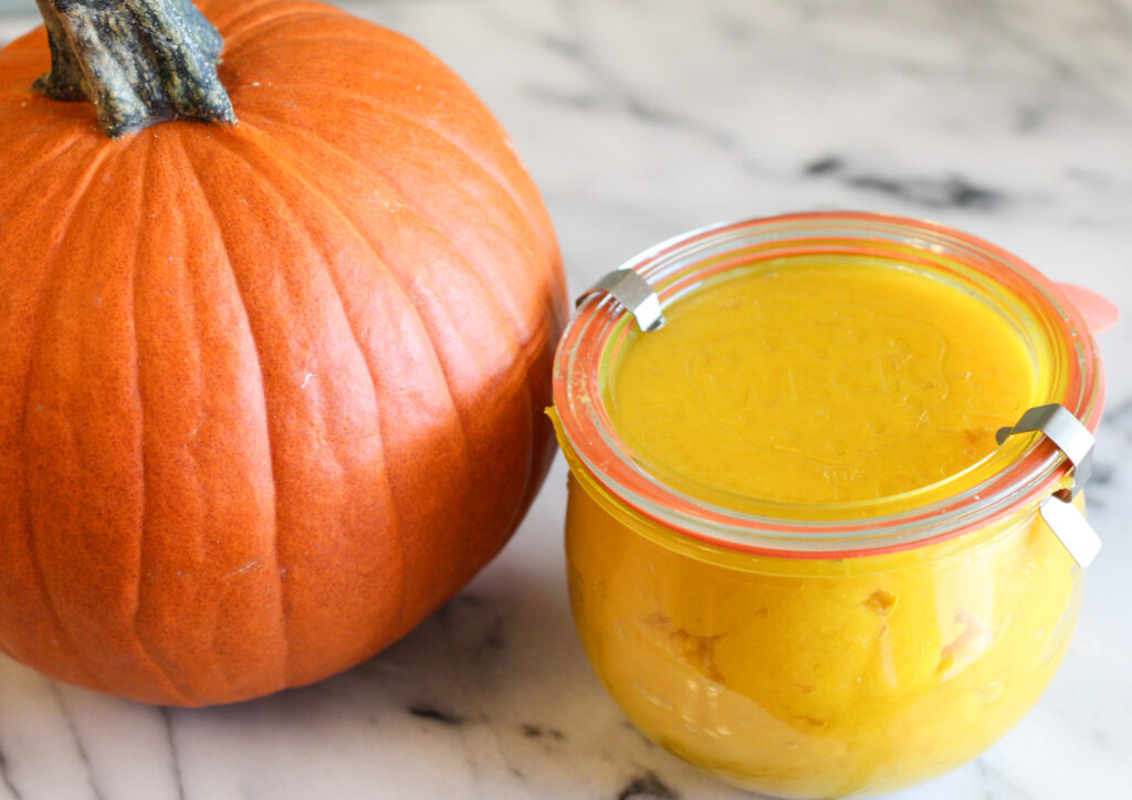 Jar of pumpkin puree next to pumpkin.