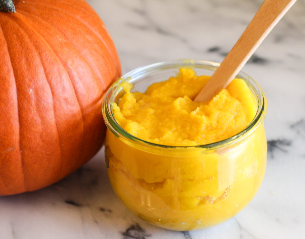Jar of pumpkin puree with small spatula in jar next to pumpkin.