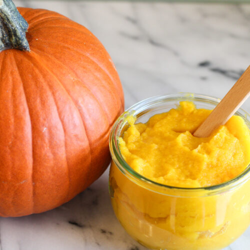 Jar of pumpkin puree with small spatula in jar next to pumpkin.