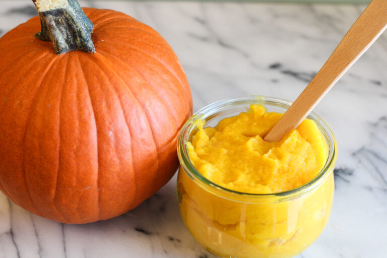 Jar of pumpkin puree with small spatula in jar next to pumpkin.