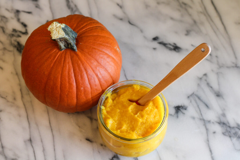 Jar of pumpkin puree with small spatula in jar next to pumpkin.