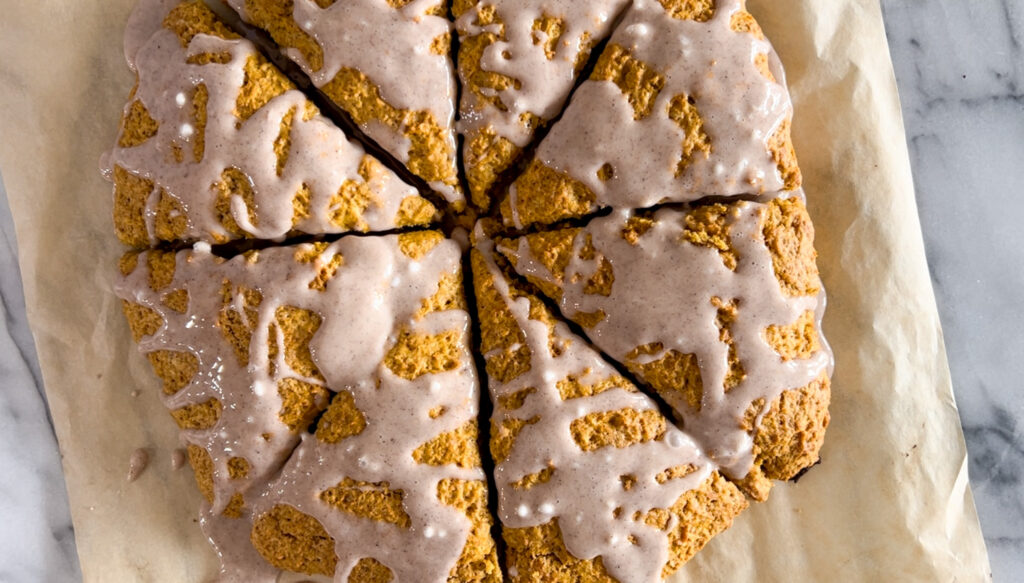 Sourdough pumpkin scones with spiced glaze on parchment paper. 