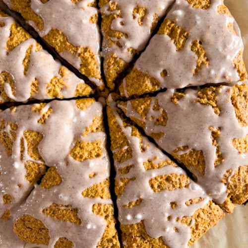 Sourdough pumpkin scones with spiced glaze on parchment paper.