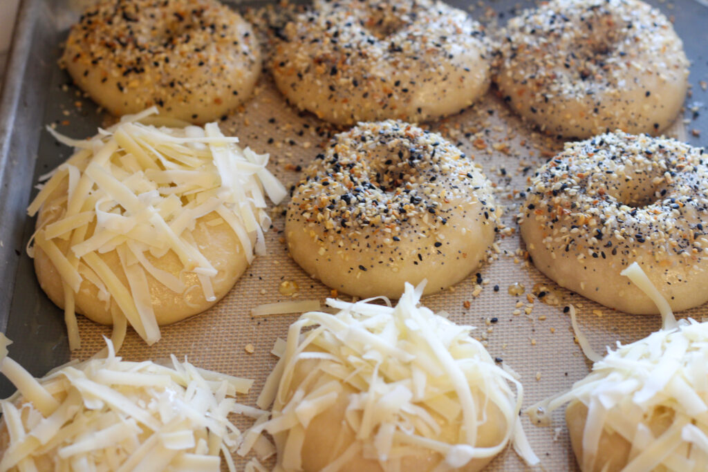 Unbaked sourdough cheese and everything bagels on baking tray.