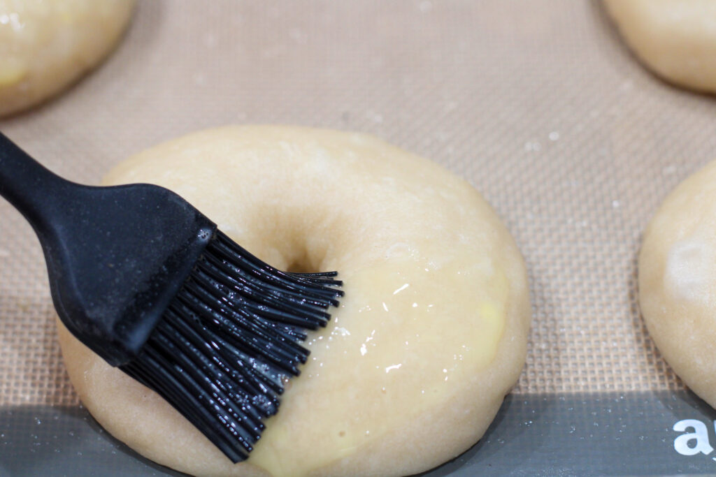 Brushing egg wash onto unbaked sourdough bagels.