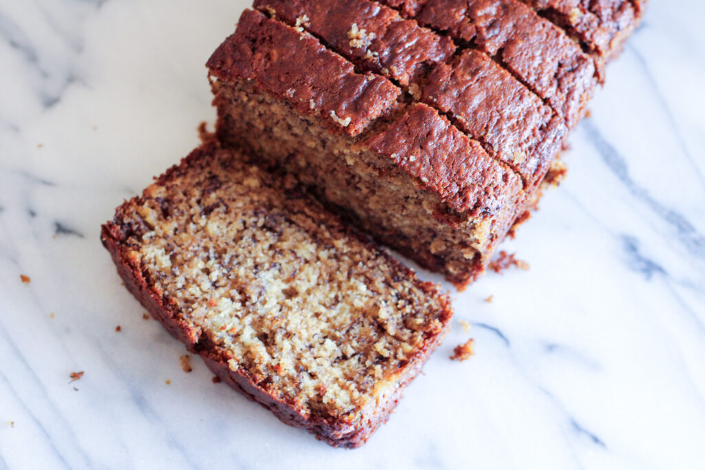 Sliced loaf of banana bread on marble countertop. 