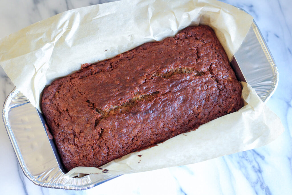 Loaf of banana bread in tin lined with parchment paper. 