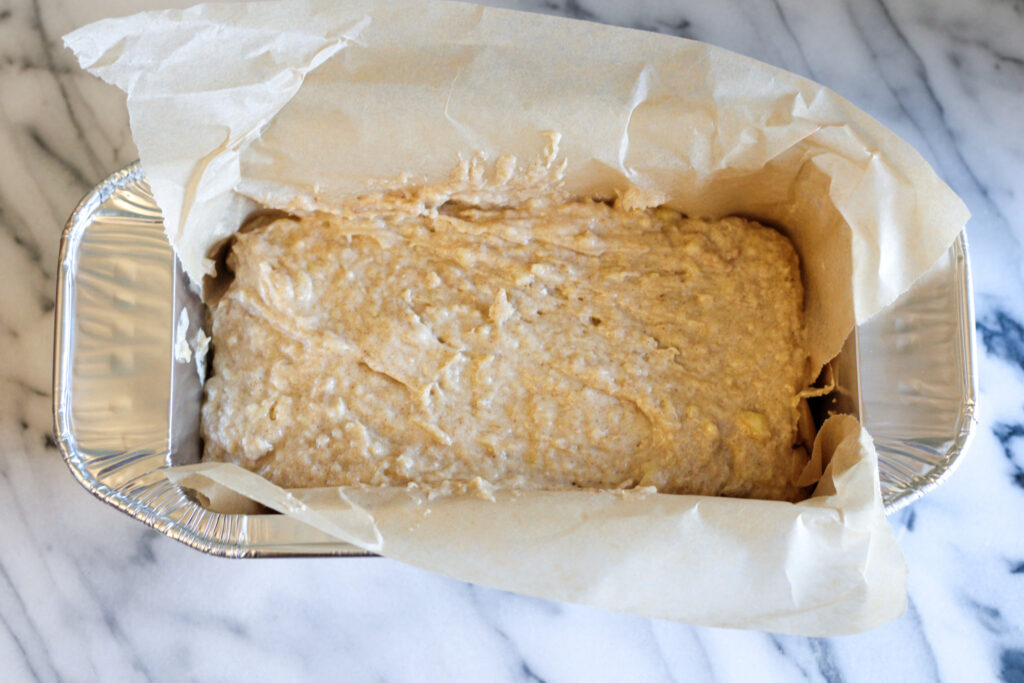 Sourdough banana bread batter in parchment paper lined loaf pan. 