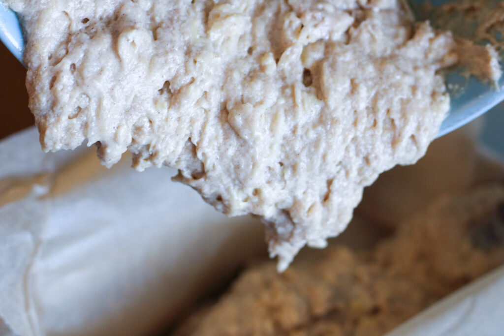 Sourdough banana bread batter pouring into loaf pan lined with parchment paper. 
