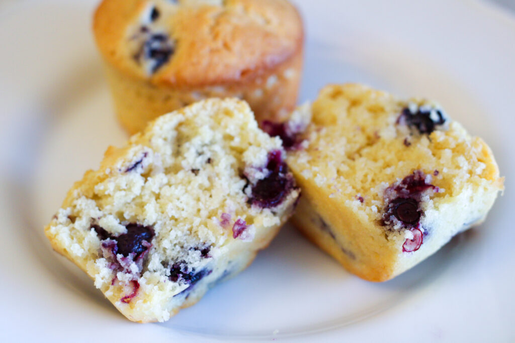 Two blueberry muffins on plate.  One is cut in half. 