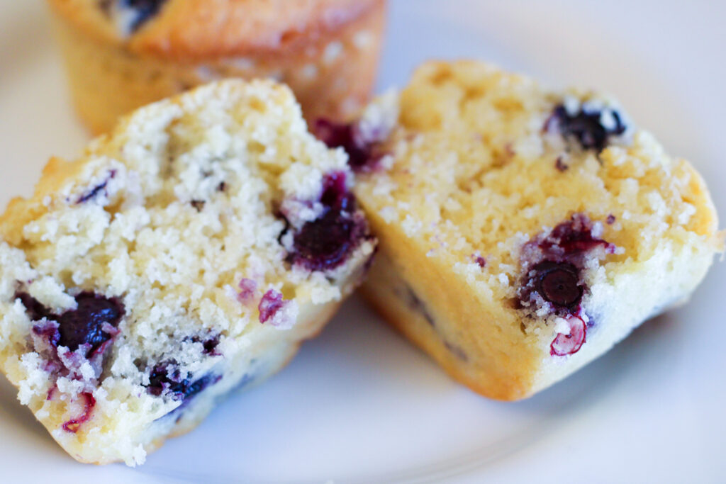 Close-up of blueberry muffin cut in half with second muffin in background. 